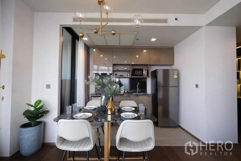 Condominium for rent in Khlong Toei, Bangkok - Modern dining room and open kitchen with brass chandelier and full-size refrigerator.