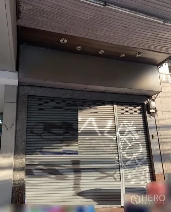 店屋 出租在Bang Rak, Bangkok - 街边店铺立面，金属卷闸门关闭，带遮檐与筒灯，位于邦拉克商圈。