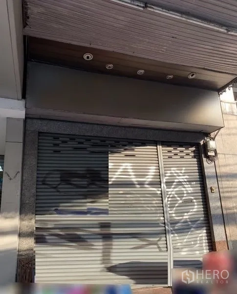 店屋 出租在Bang Rak, Bangkok - 街边店铺立面，金属卷闸门关闭，带遮檐与筒灯，位于邦拉克商圈。