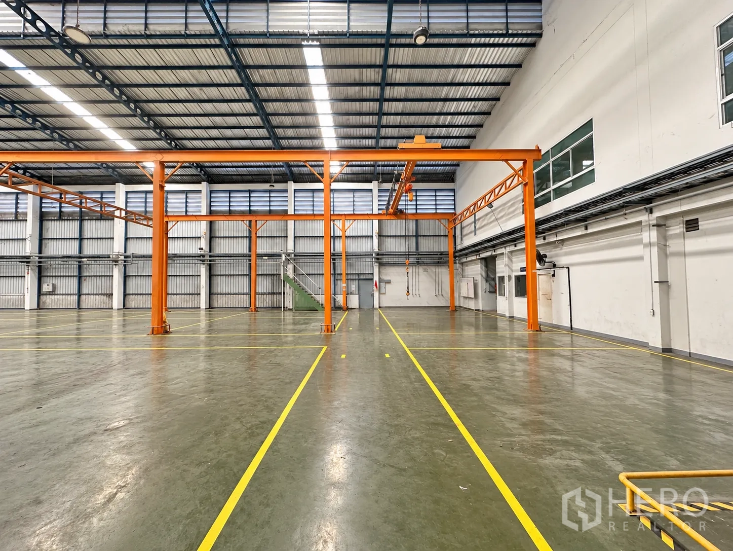 Factory for sale in Lam Luk Ka, Pathum Thani - Spacious factory hall with orange overhead crane, epoxy flooring, and safety lines.