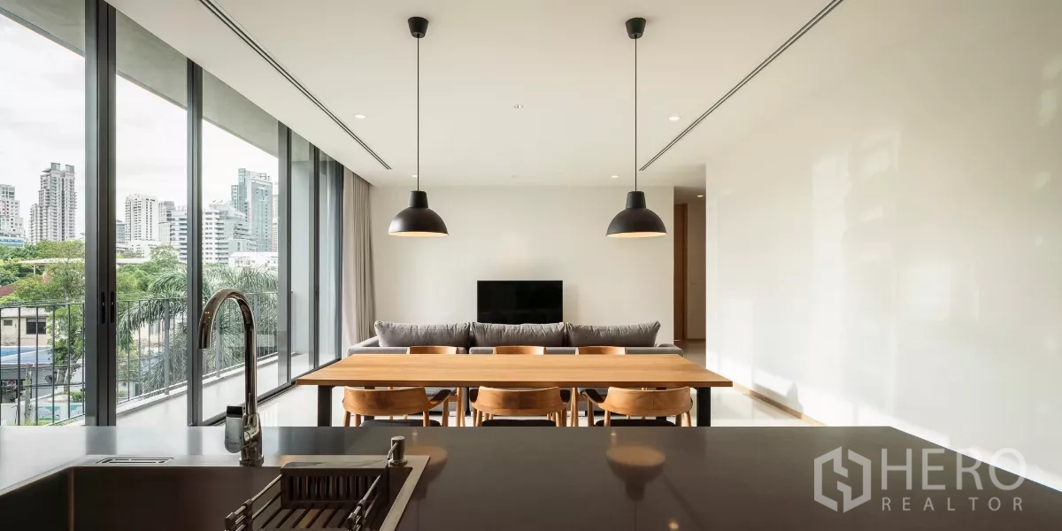 公寓 出租在Bang Kapi, Bangkok - 从厨房岛台望向客餐厅，整面落地窗、沙发与电视。