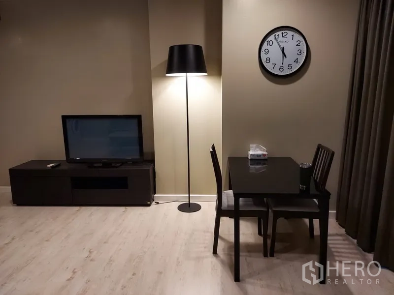 Condominium for rent in Phaya Thai, Bangkok - Dining nook for two with floor lamp, wall clock and TV console in the living area.