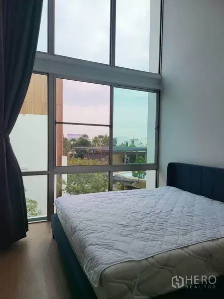 Detached House for rent in Saphan Sung, Bangkok - Cozy bedroom with double‑height floor‑to‑ceiling windows, dark curtains and views over trees and neighboring homes.