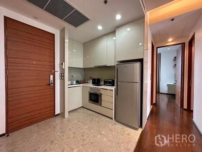 公寓 出租在Khlong Toei, Bangkok - L形厨房，亮面橱柜、嵌入式烤箱与大冰箱，靠近玄关。