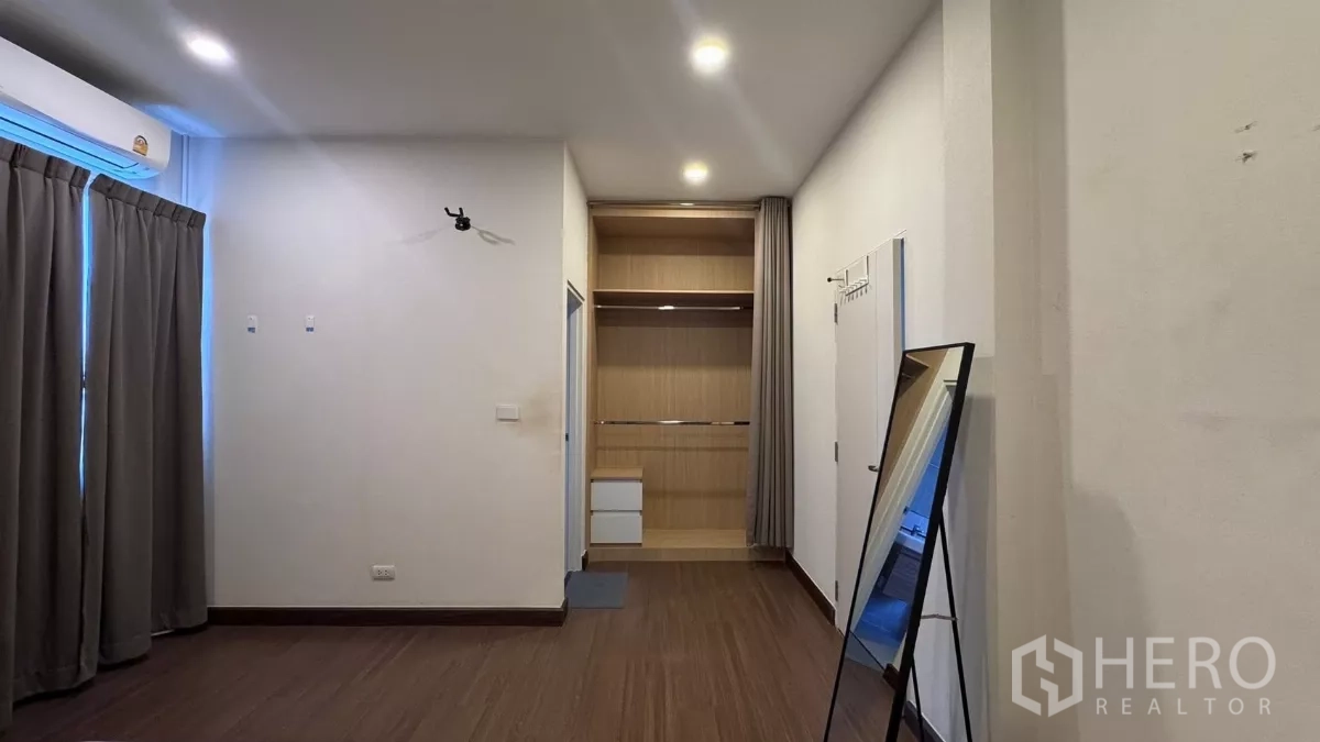 Detached House for rent or sale in Saphan Sung, Bangkok - Large bedroom with built‑in open closet, freestanding mirror and dark blackout curtains.