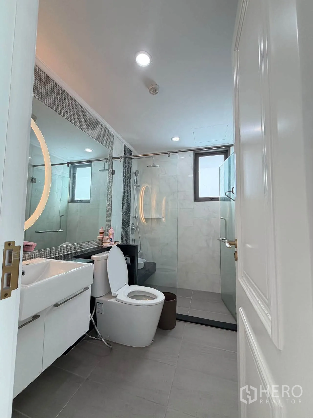 Condominium for sale in Watthana, Bangkok - Contemporary bathroom with vanity, toilet, and glass-enclosed rain shower.