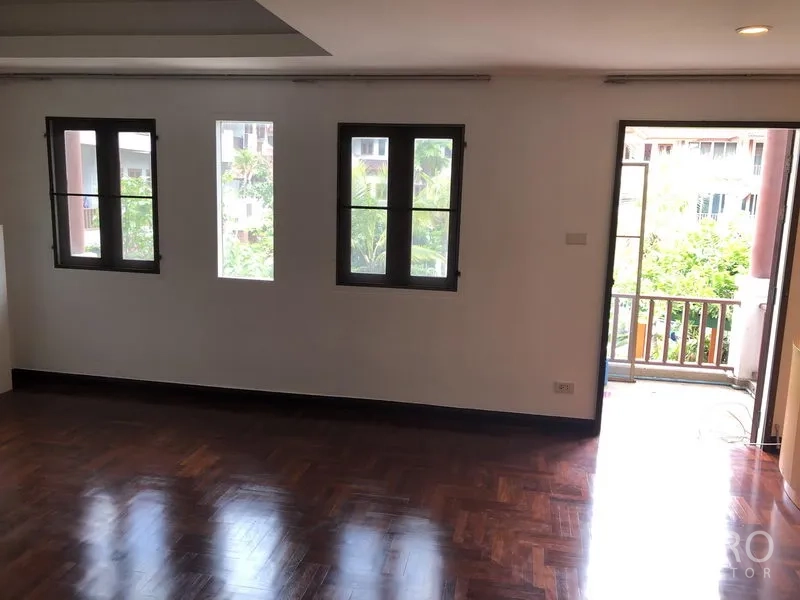Townhouse for rent or sale in Watthana, Bangkok - Upper-floor bedroom with polished wood floors, three windows and a small balcony.