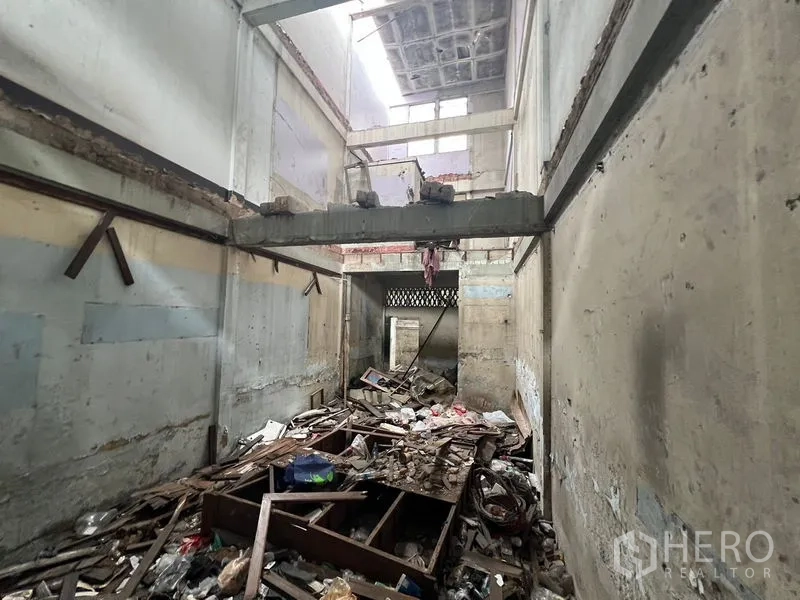 Land for rent in Watthana, Bangkok - Interior of a derelict structure showing debris, exposed beams, and high ceilings.