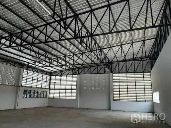 Warehouse for rent in Lam Luk Ka, Pathum Thani - Spacious warehouse interior featuring a high steel truss roof and louvered ventilation windows.
