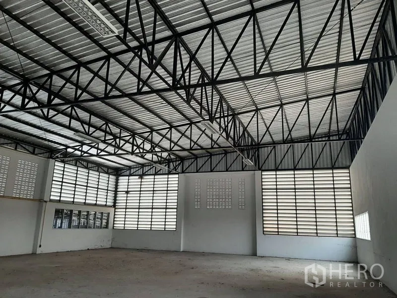 Warehouse for rent in Lam Luk Ka, Pathum Thani - Spacious warehouse interior featuring a high steel truss roof and louvered ventilation windows.