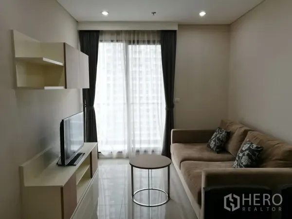 Condominium for rent in Ratchathewi, Bangkok - Living room with sofa, TV cabinet and sliding glass door opening to a light‑filled balcony.