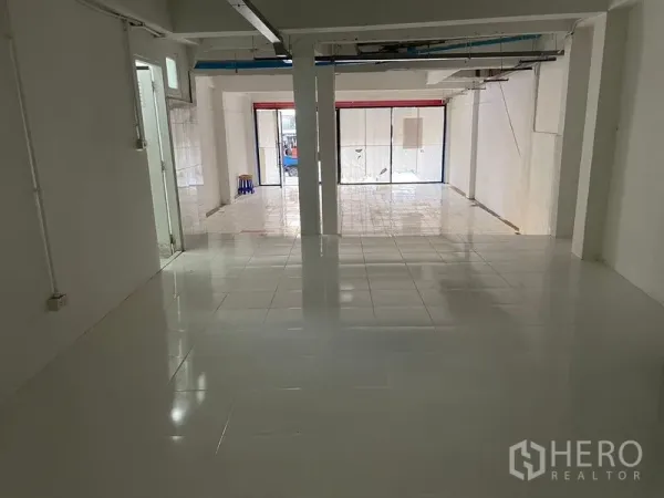 Shophouse for rent in Watthana, Bangkok - Open-plan shophouse ground floor with white tiles, support columns, and a wide glass storefront facing the street.