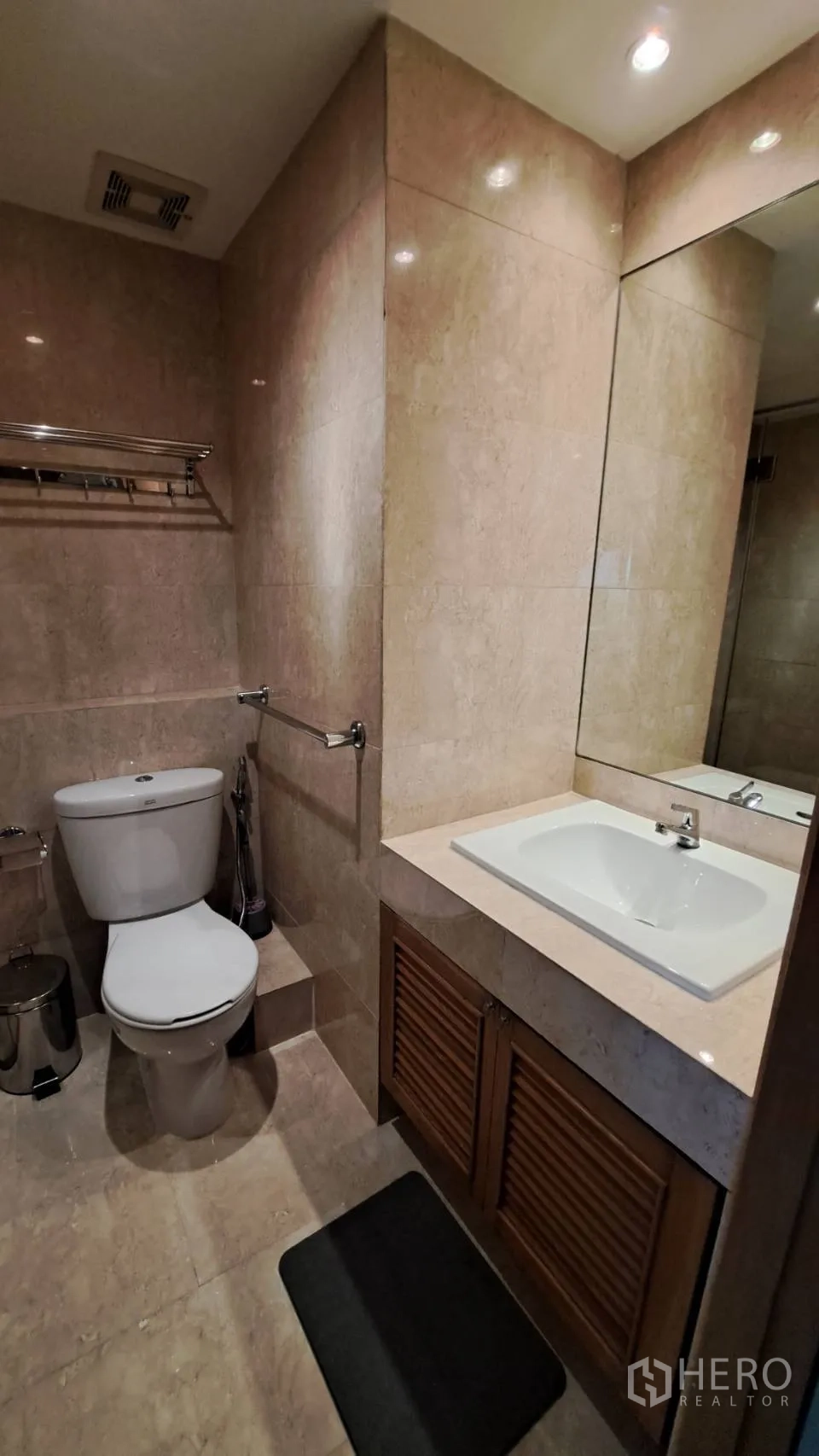 Condominium for rent in Khlong Toei, Bangkok - Bathroom vanity with large mirror, sink, and stone-tiled walls.