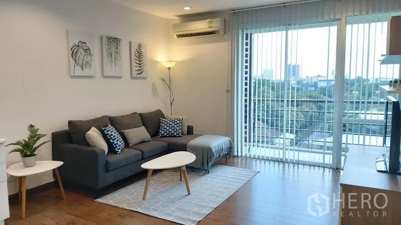 Condominium for rent in Phra Khanong, Bangkok - Open-plan lounge with balcony and city view through full-height sliding doors, TV console and air conditioner.