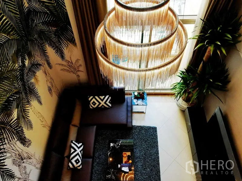 Condominium for sale in Sathon, Bangkok - Top view of the living room showing layered chandelier, sectional sofa and tall windows.