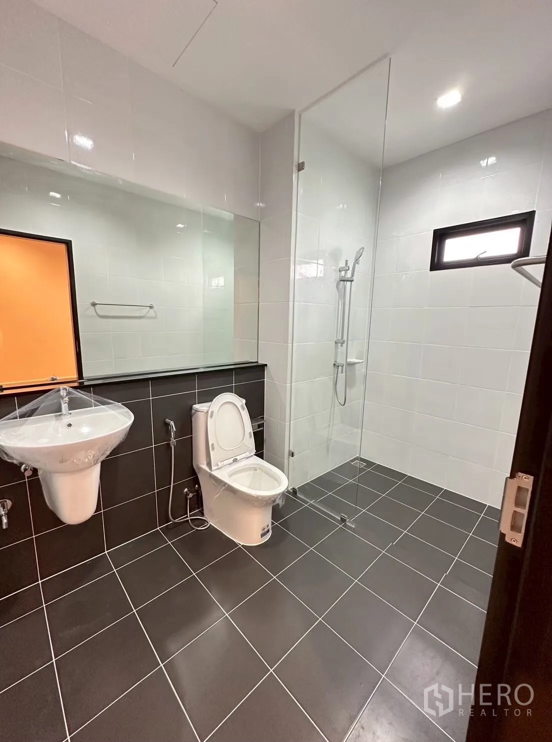 Home Office for rent in Lat Phrao, Bangkok - Modern bathroom with glass-enclosed shower, wall-length mirror, and black floor tiles.