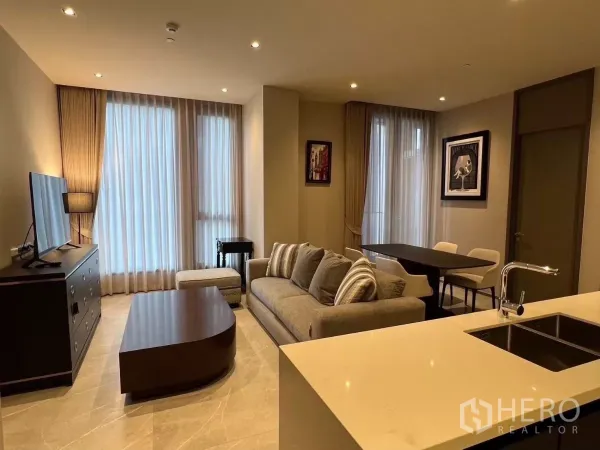 公寓 出租在Watthana, Bangkok - 温馨灯光的客厅，配有沙发、电视柜、茶几与落地纱帘。