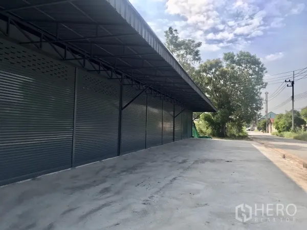 Warehouse for rent in Lam Luk Ka, Pathum Thani - Covered loading bay with roller doors beside a quiet street and wide concrete forecourt.