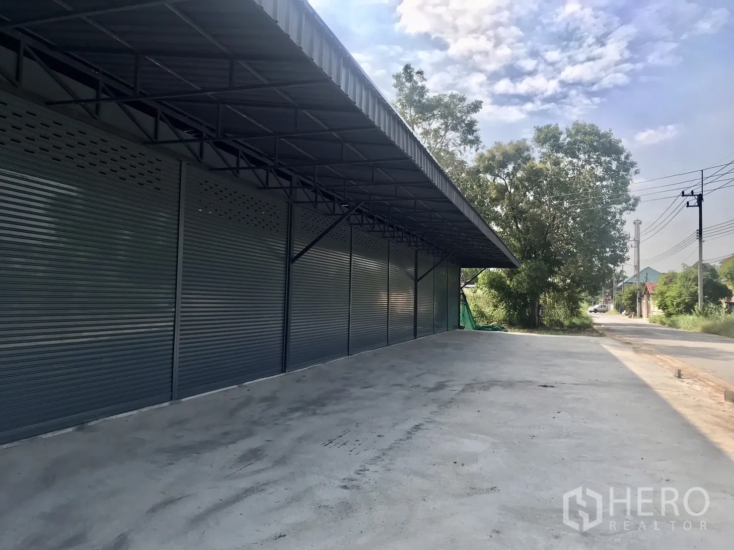 Warehouse for rent in Lam Luk Ka, Pathum Thani - Covered loading bay with roller doors beside a quiet street and wide concrete forecourt.