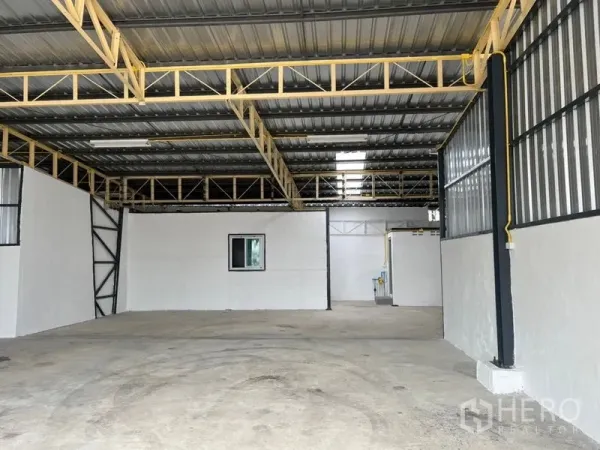 Warehouse for rent in Suan Luang, Bangkok - Open-plan storage hall with high ceiling, internal office section, and metal cladding panels.