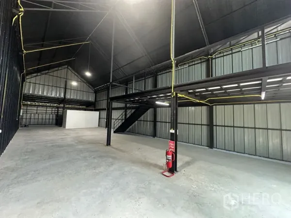 Warehouse for rent in Bueng Kum, Bangkok - High-ceiling steel-frame warehouse interior with mezzanine, concrete floor and industrial lighting.
