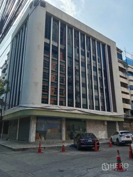带办公室的家 出租在Watthana, Bangkok - 中高层商业建筑外立面，竖向玻璃窗格，前方街边停车位。