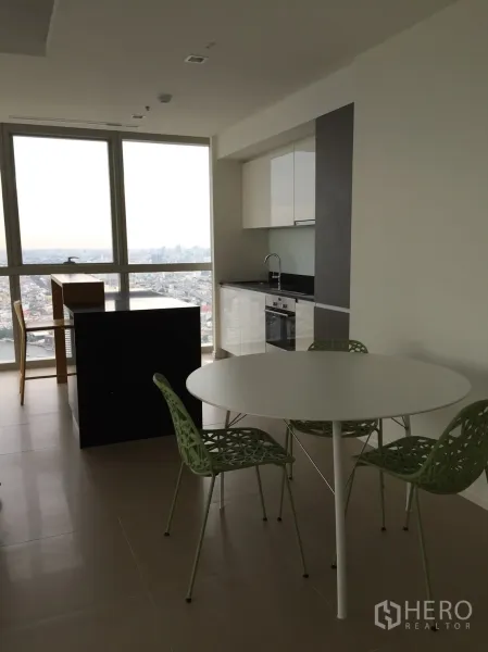 Condominium for rent or sale in Khlong San, Bangkok - Modern open kitchen with island and round dining set overlooking the skyline through large windows.