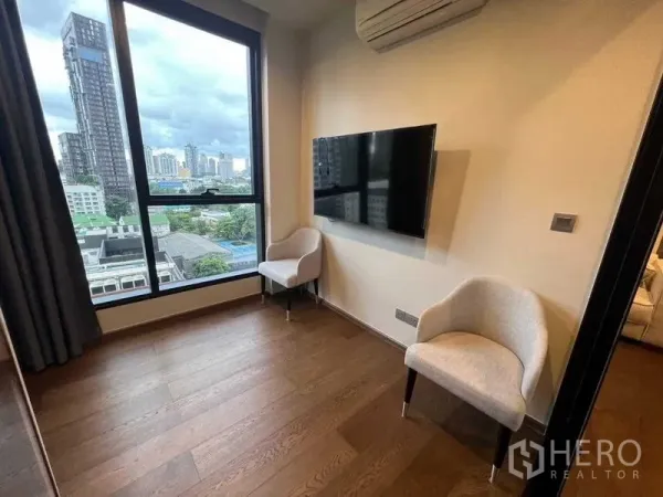 公寓 出租在Khlong Toei, Bangkok - 转角房配两把单椅、壁挂电视和大窗，可欣赏城市景色。