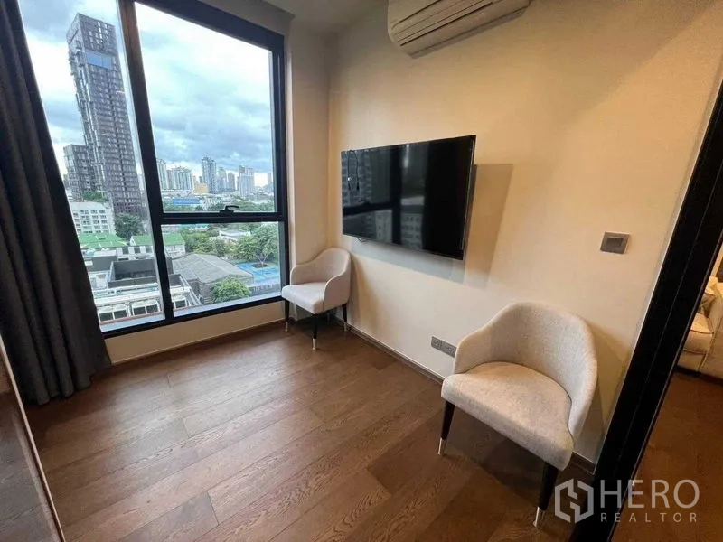 公寓 出租在Khlong Toei, Bangkok - 转角房配两把单椅、壁挂电视和大窗，可欣赏城市景色。