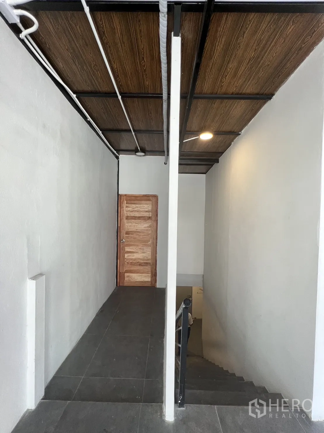 Retail Space for rent in Watthana, Bangkok - Hallway with dark tiles and a wooden door beneath a wood-look ceiling.