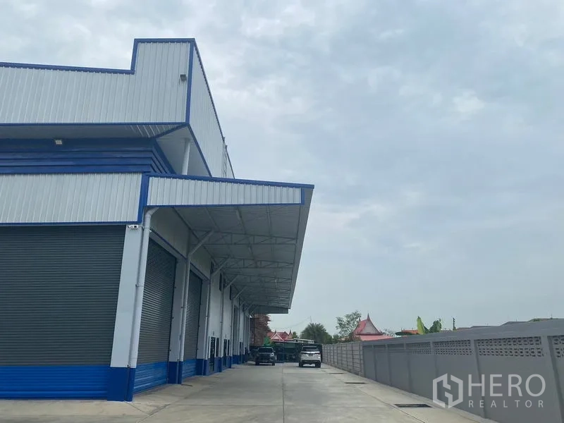Warehouse for rent in Pathum Thani - Front canopy with several loading bays and a broad concrete apron beside the boundary wall.