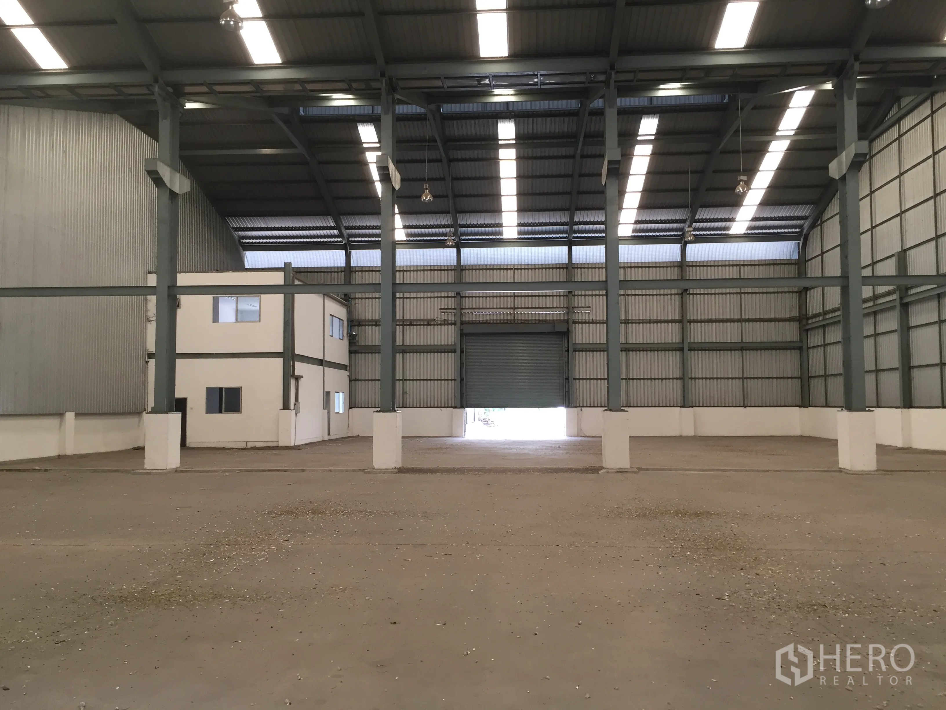 Factory for rent in Khlong Luang, Pathum Thani - Open production space with high-bay lighting and a rear roller shutter door.