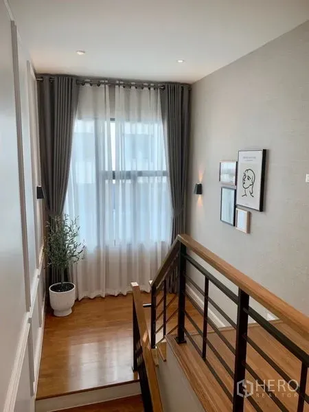 Detached House for sale - Bright stair landing with wood steps, black metal railing, large curtained window and framed wall art.
