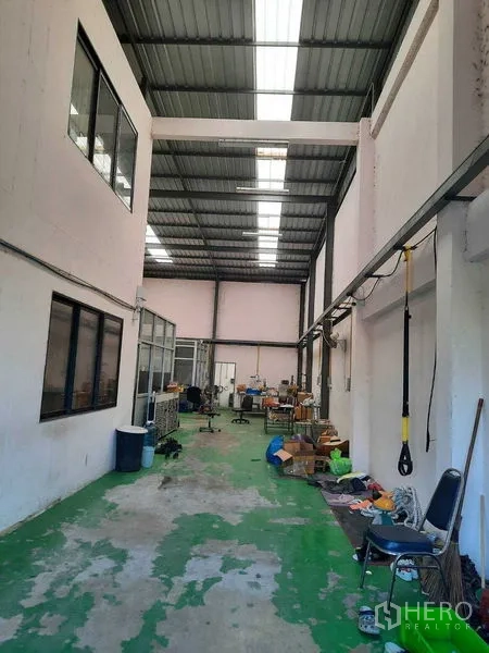 Warehouse for sale in Samut Prakan - Open warehouse hall with a high steel roof, skylight panels and a green coated floor.