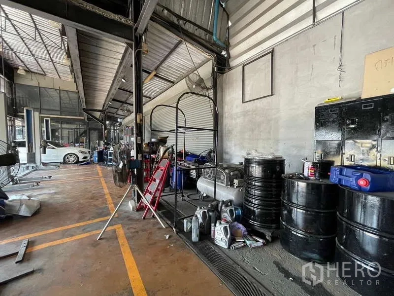 Warehouse for rent in Lat Phrao, Bangkok - Open warehouse interior with a high steel roof, roller door and storage drums along the wall.