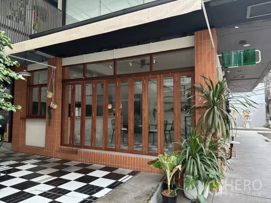Retail Space for rent in Watthana, Bangkok - Corner retail facade with brick columns, folding wooden-framed glass doors, awning and a black-and-white checkerboard patio.