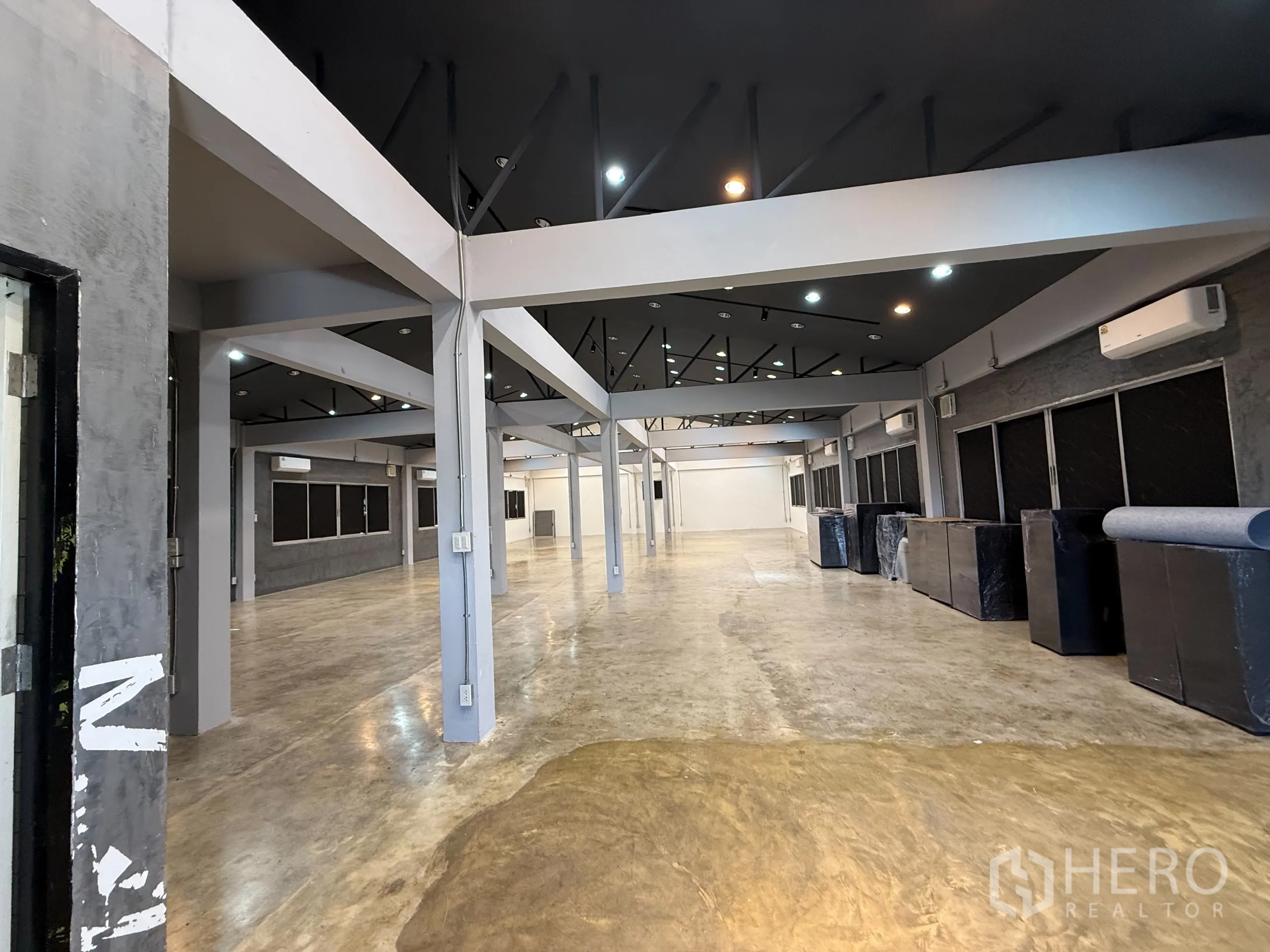 办公空间 出租在Wang Thonglang, Bangkok - 大面积工作区斜角视图，外露桁架、轨道灯、多台空调与灰色墙面窗户。