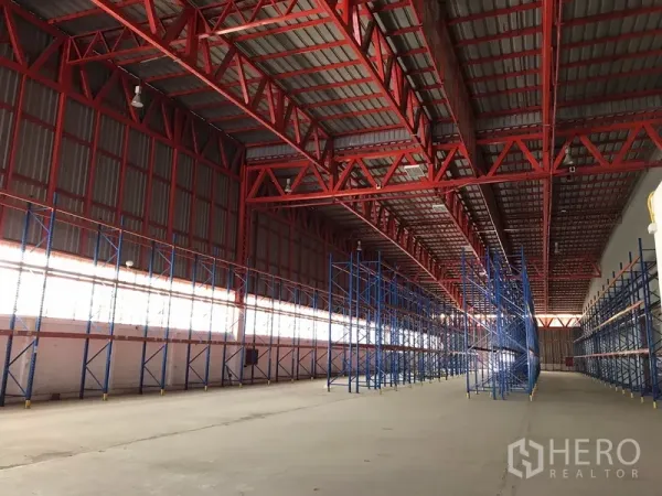 Warehouse for rent in Bang Na, Bangkok - Wide warehouse interior with long rows of blue pallet racking beneath red steel roof.