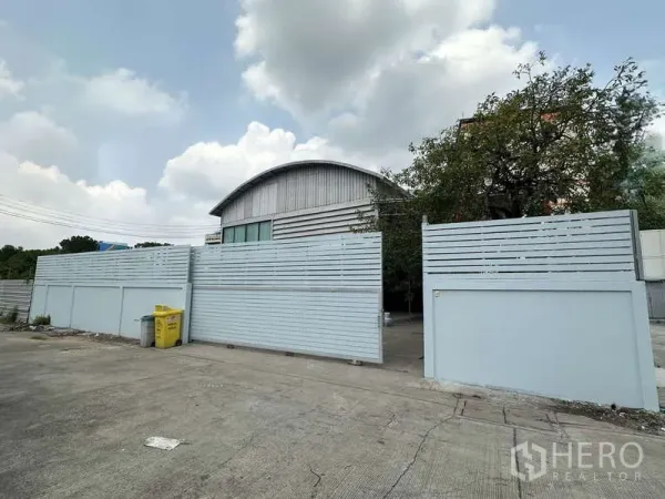 Warehouse for rent in Pak Kret, Nonthaburi - Secure gated standalone warehouse with high concrete fence and wide driveway.