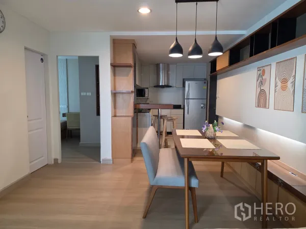 Condominium for rent in Huai Khwang, Bangkok - Open-plan dining room with pendant lights, bench seating, and kitchen in the background.
