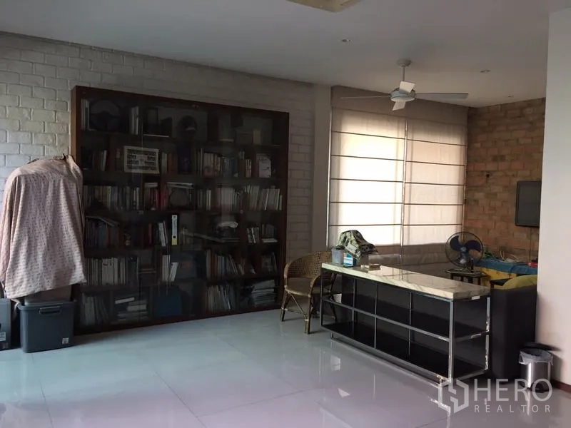 Home Office for rent or sale in Bang Rak, Bangkok - Study room with a large bookcase, sofa, ceiling fan and glossy white flooring.