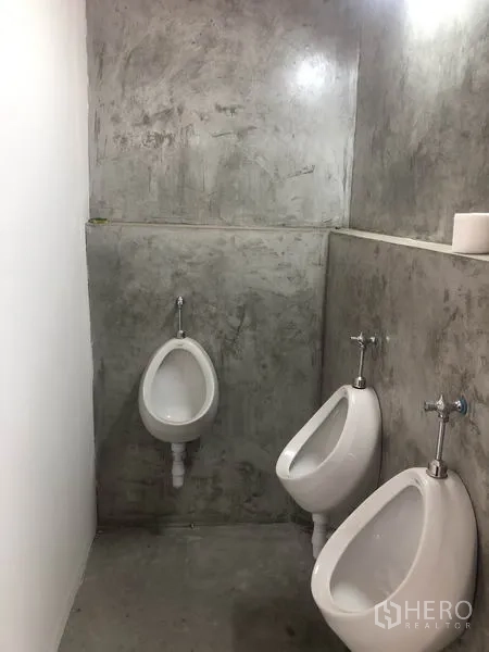 Warehouse for rent in Bang Yai, Nonthaburi - Men’s restroom area with two wall‑mounted urinals and concrete finish.