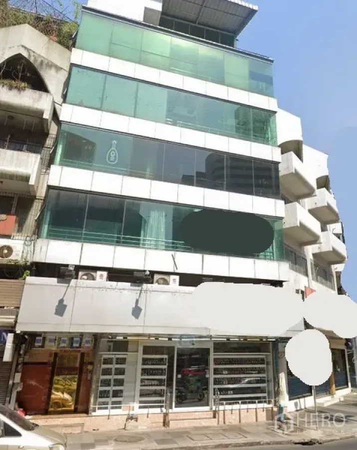 Retail Space for rent in Watthana, Bangkok - Street view of a mid-rise commercial building with green-tinted glass facade and a wide ground-floor retail frontage in Watthana, Bangkok.