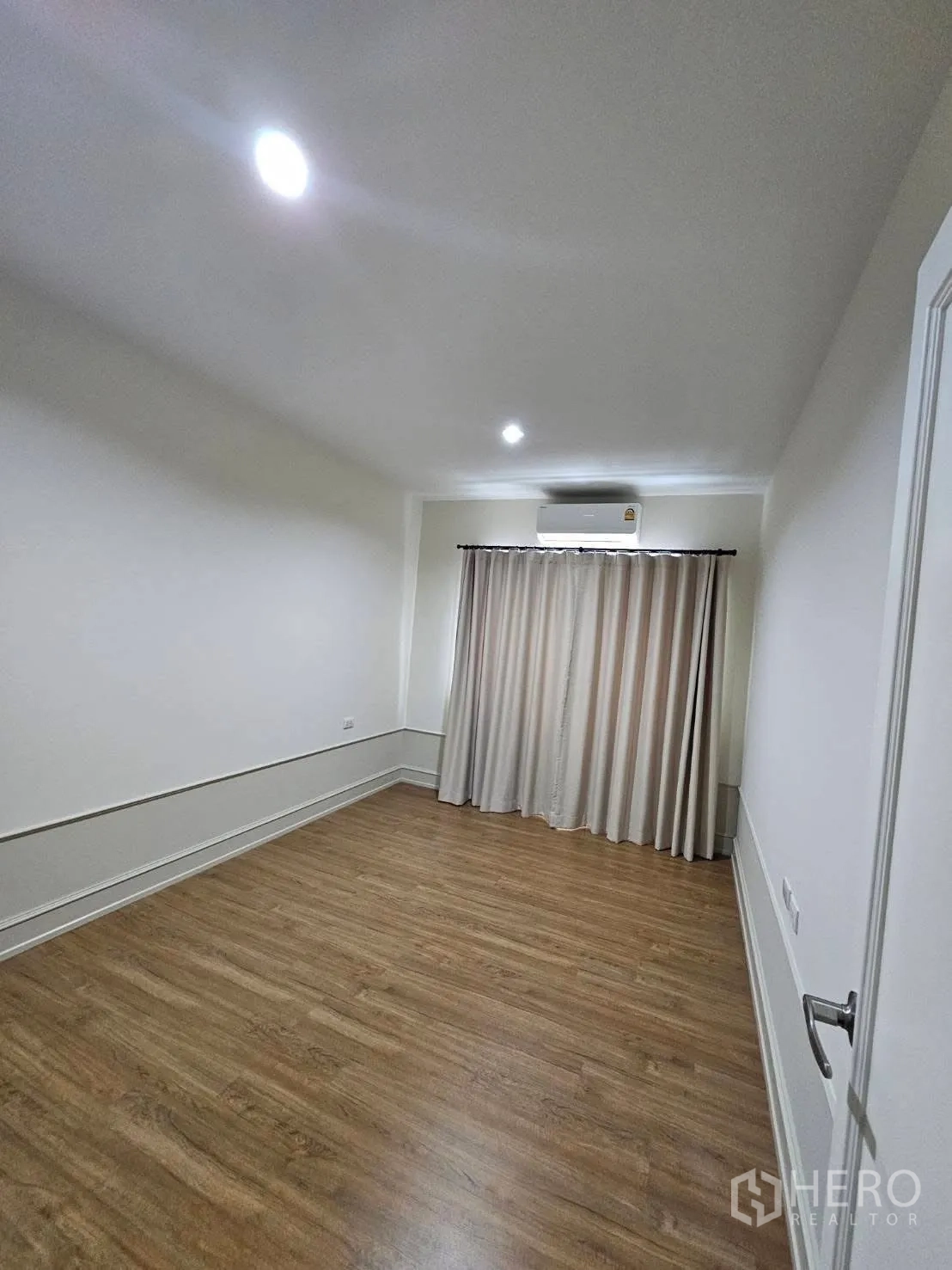 Townhouse for rent in Saphan Sung, Bangkok - Empty third bedroom with wood floors, curtained window, and ceiling spotlights.