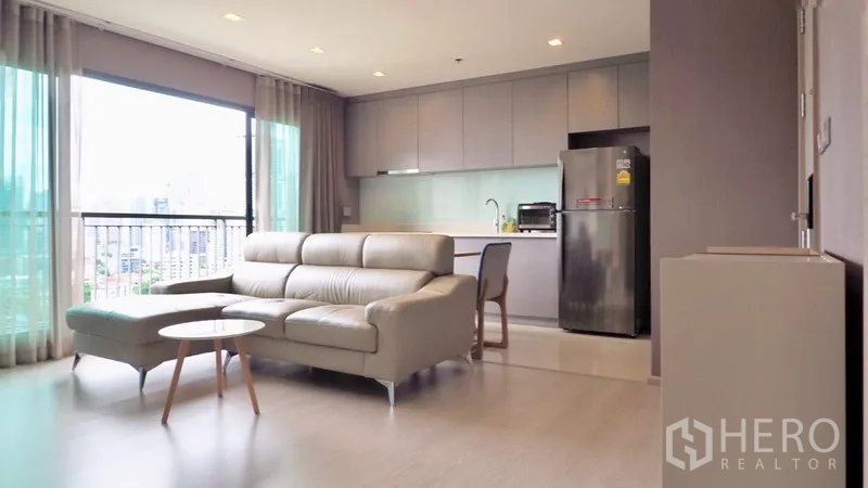 Condominium for rent in Khlong Toei, Bangkok - Open-plan lounge with floor-to-ceiling windows and fitted kitchen with stainless fridge.