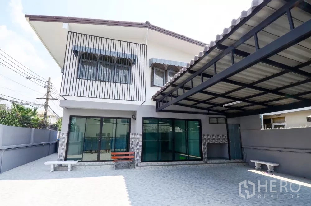 带办公室的家 出租在Lat Phrao, Bangkok - 两层转角住办合一建筑，带遮棚车位、推拉玻璃门与铺砖前院。
