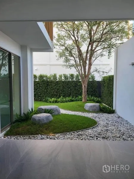 Detached House for rent in Saphan Sung, Bangkok - Landscaped private courtyard with tree, curved stone path, pebbles and trimmed hedges beside a covered terrace.