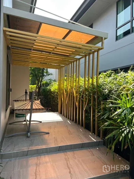 Detached House for rent in Bang Kapi, Bangkok - Covered patio with modern pergola beside landscaped greenery and hammock stand.