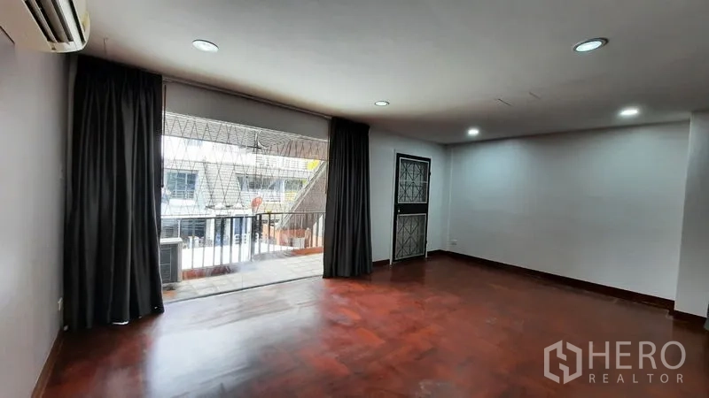 Townhouse for rent or sale in Suan Luang, Bangkok - Large living room opening to a balcony with sliding glass doors and curtains.