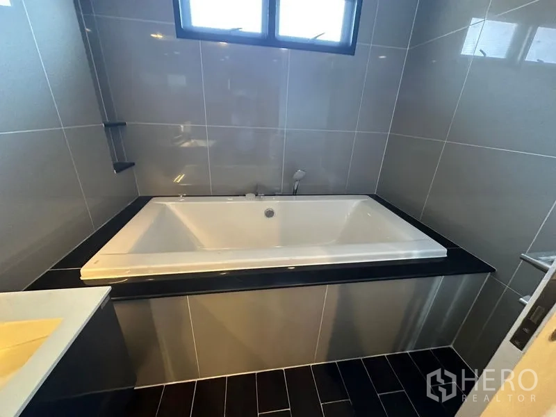 Detached House for rent or sale in Lam Luk Ka, Pathum Thani - Bathroom featuring a soaking bathtub set in a tiled surround beneath a window.